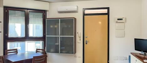 Una habitación con una mesa de comedor, sillas, un armario, una puerta y un televisor.