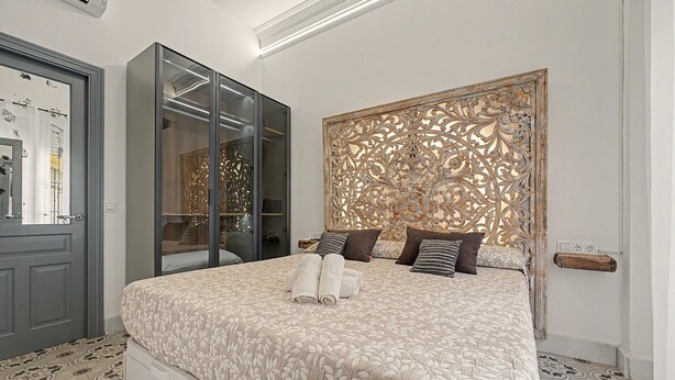 A hotel room with a bed, a wardrobe, a decorative headboard, and a door with a mirror. - El Mar Azul 5 Beachfront Family Apartment (Torremolinos)