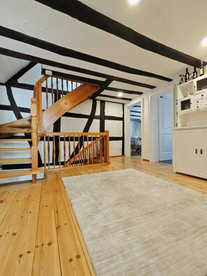 A spacious loft with exposed beams, a wooden staircase, and a kitchen area.