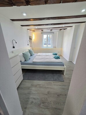 Une chambre à coucher comprenant un lit, des tables de chevet, une fenêtre et un plafond avec des poutres apparentes.