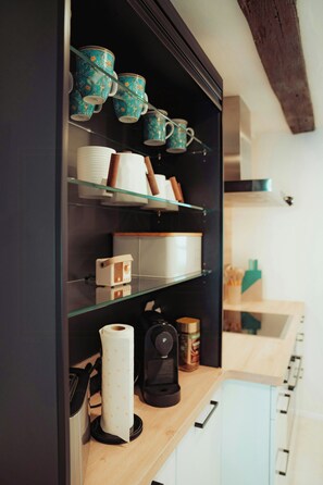 Eine Küche mit einem schwarzen Schrank, der verschiedene Gegenstände wie eine Kaffeemaschine, Tassen und eine Küchenrolle beherbergt.