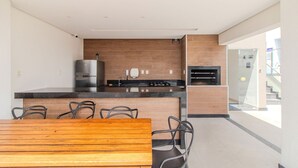 A modern kitchen with a built-in oven, a refrigerator, and a dining area with a wooden table and chairs. - Apartment in a Condominium in Setor Bueno Lhd0403 (Goiânia)