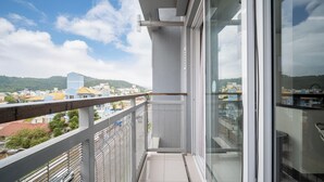 Varanda com guarda-corrimão de metal, porta de vidro e vista para um horizonte urbano com edifícios e colinas ao fundo.
