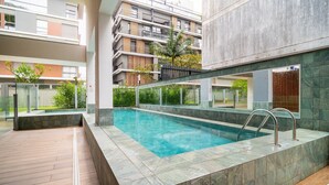 Piscina interior moderna com água cristalina, rodeada por um deck revestido de azulejos e barreiras de vidro.