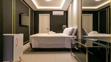 A modern hotel room with a bed, a minibar, a mirror, and a ceiling light.