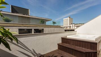 Une terrasse sur le toit avec un jacuzzi, un immeuble moderne et un ciel dégagé.