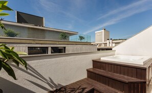 Une terrasse sur le toit avec un jacuzzi, un immeuble moderne et un ciel dégagé.