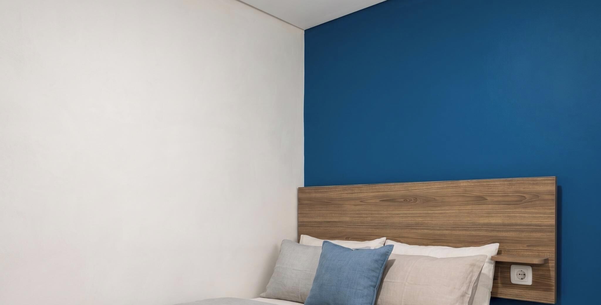 A bed with a wooden headboard against a blue wall, accompanied by pillows.