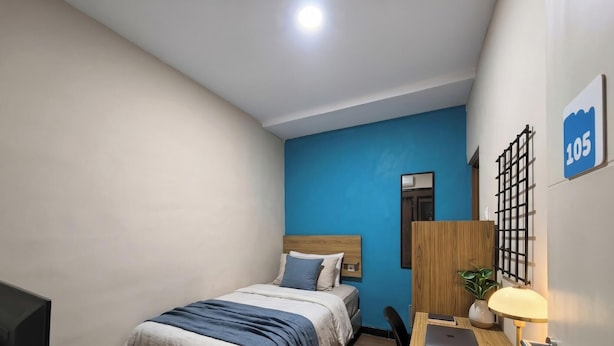 A bedroom with a bed, a desk, a chair, a lamp, and a blue wall.
