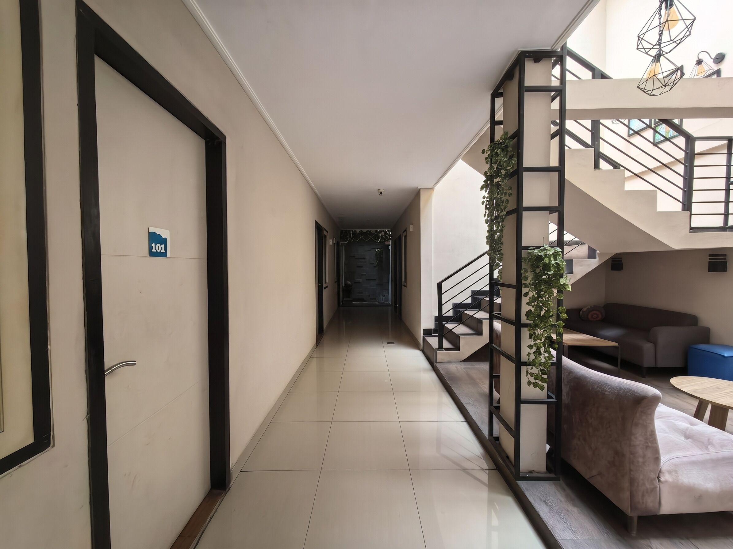 Corredor de hotel com escada, sofá e planta.