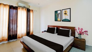 A hotel room with a bed, curtains, a wall-mounted air conditioner, a bedside table with a phone, and a vase with flowers. - Collection O Bus Terminal Haldwani (Haldwani)