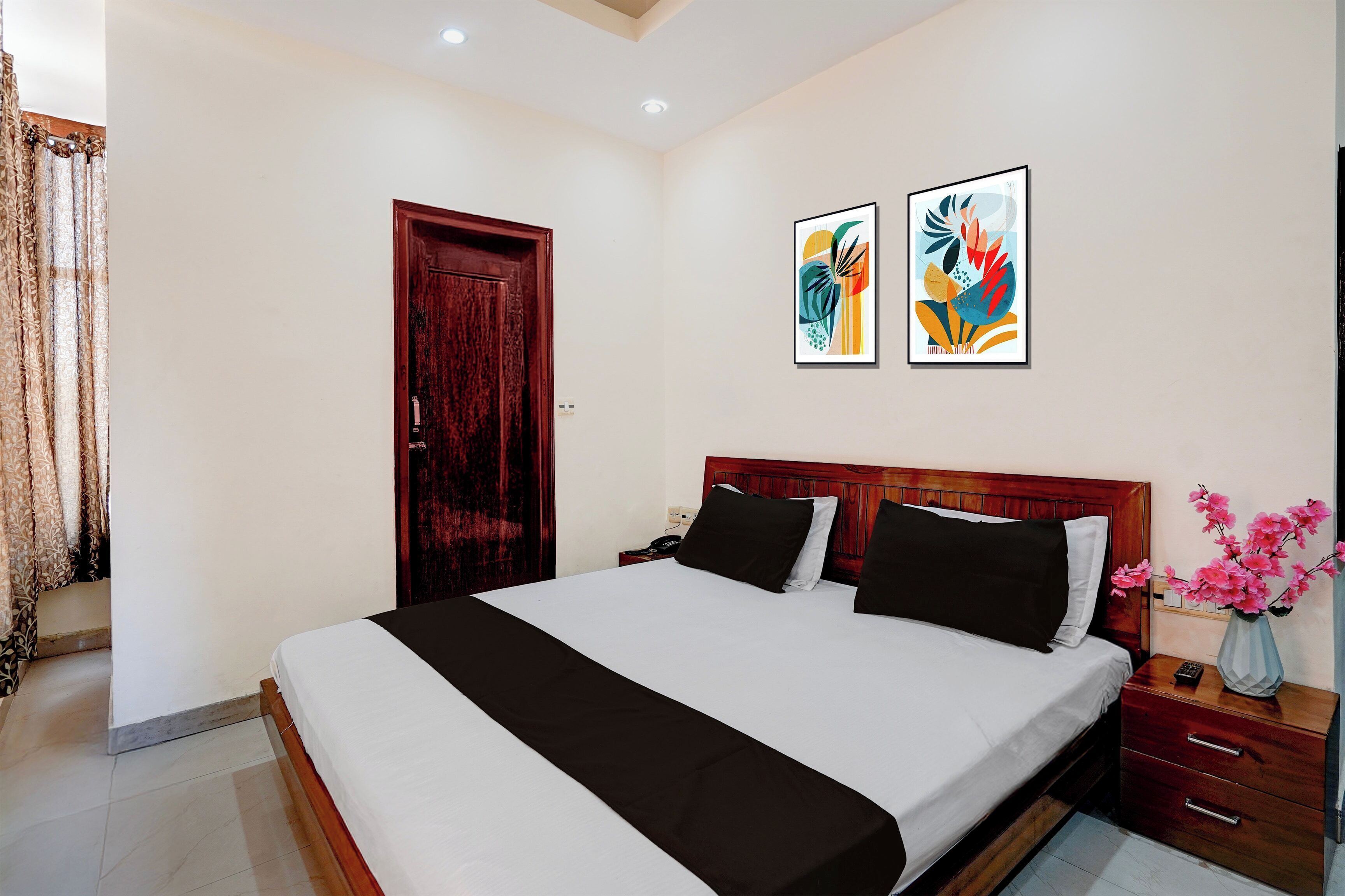 Una habitación de hotel con cama, mesita de noche y un florero con flores.