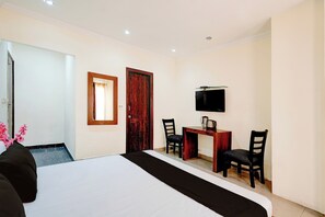 Una habitación de hotel con cama, escritorio, silla, televisor y puerta.