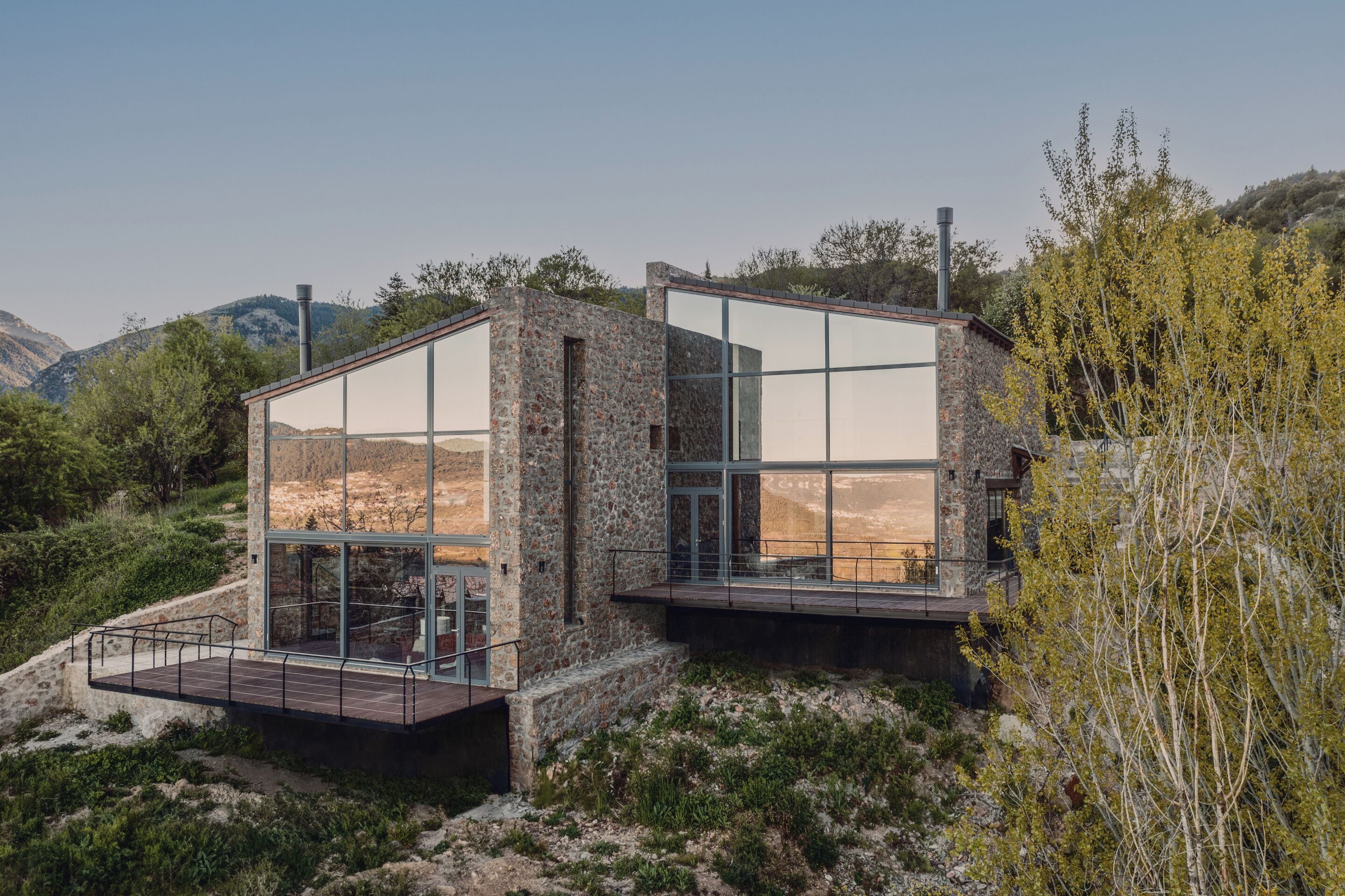 Una casa moderna con amplios ventanales, fachada de piedra y terraza de madera.