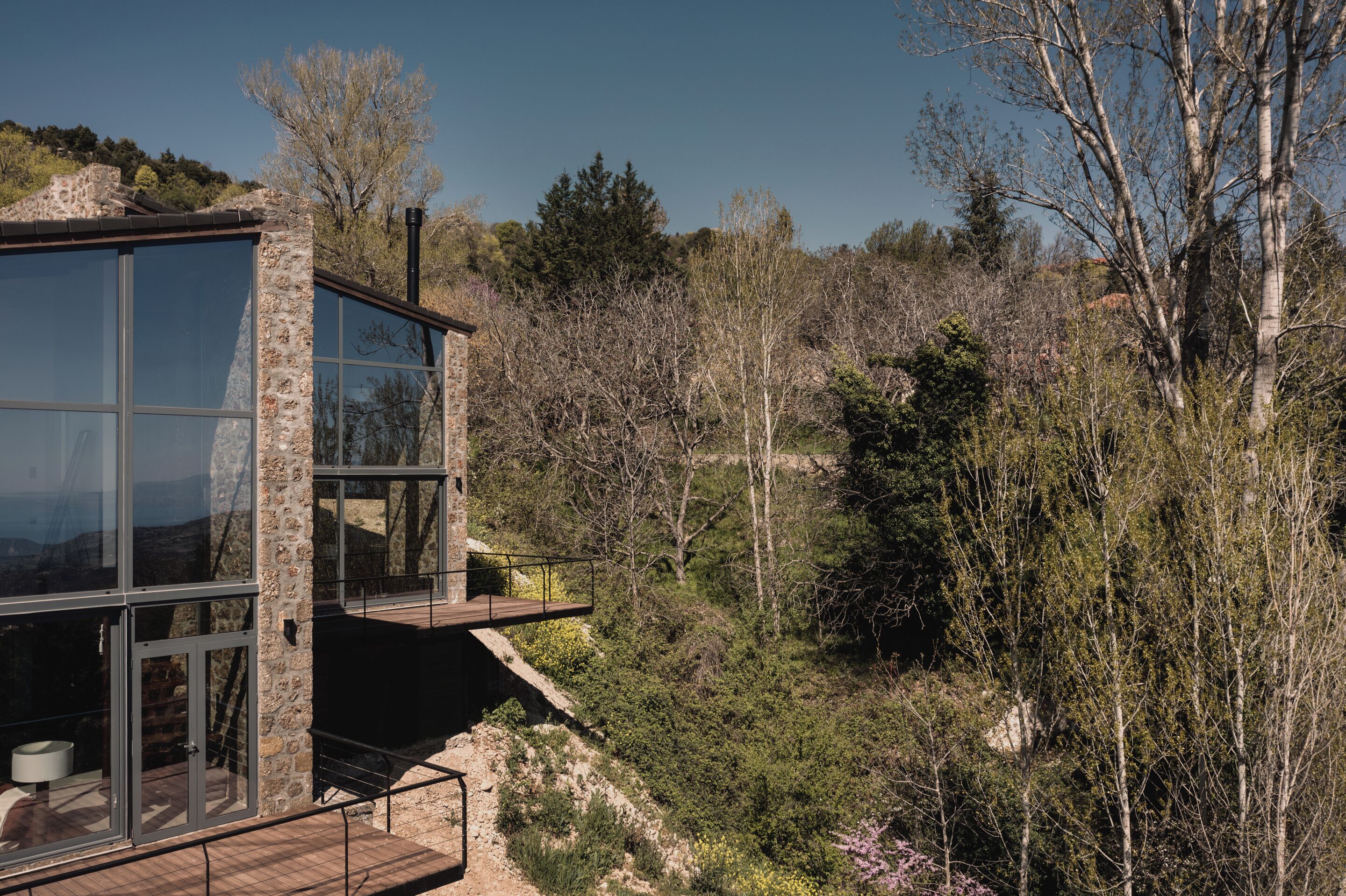 Un edificio moderno con grandes ventanales y un balcón con vistas a un área boscosa.