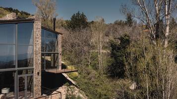Un edificio moderno con grandes ventanales y un balcón con vistas a un área boscosa.