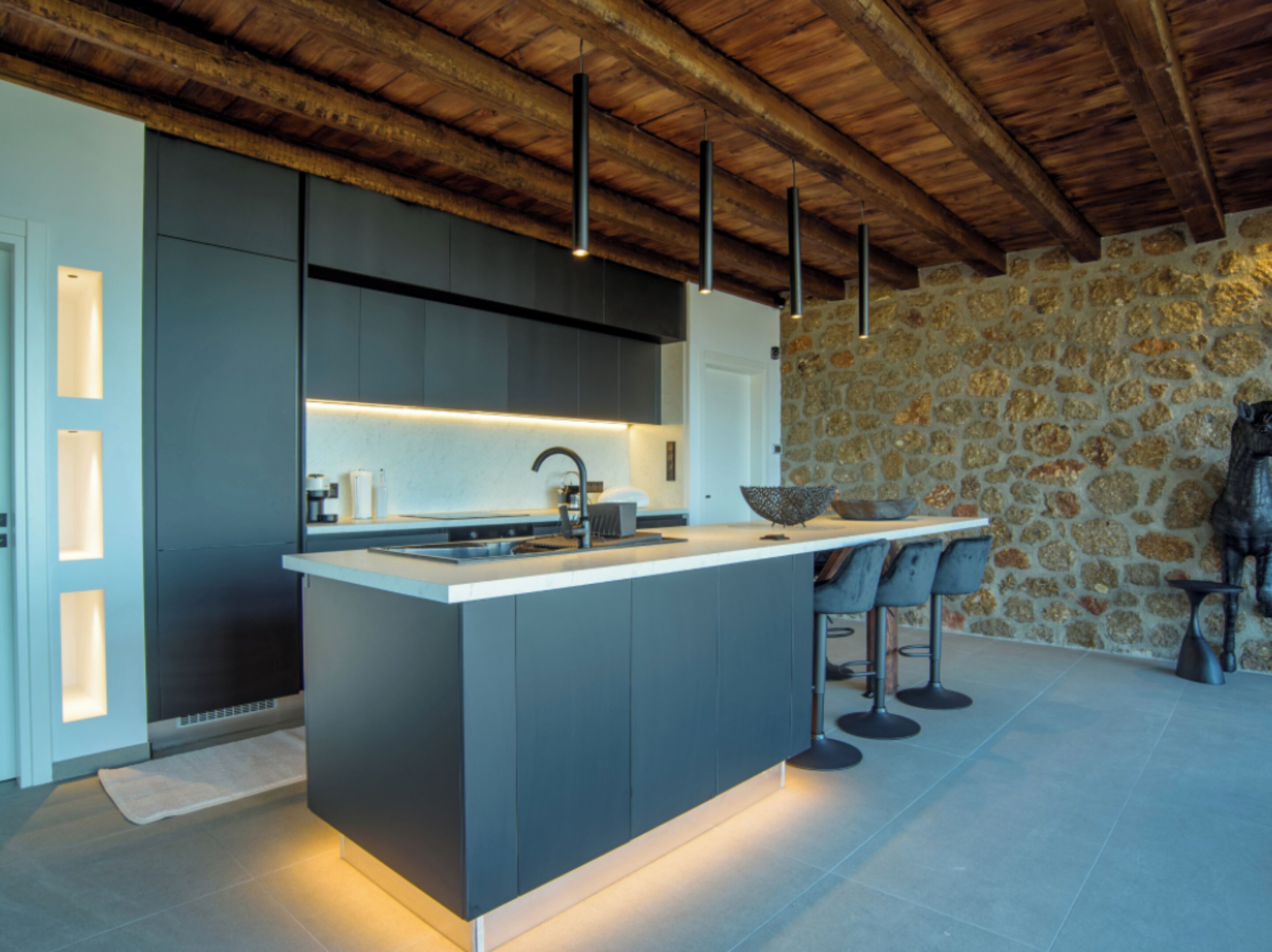 Una cocina moderna con una isla central, taburetes de bar y una pared de piedra.