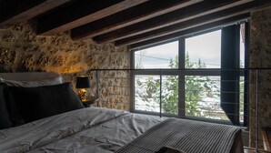 A bedroom with a large window, a bed, a bedside table with a lamp, and a stone wall. - Heartbeat Mountain Escapes (Kato Sinikia Trikalon)