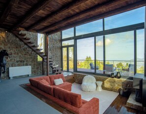 A spacious living area with a large window, a stone wall, a staircase, and a red sofa.