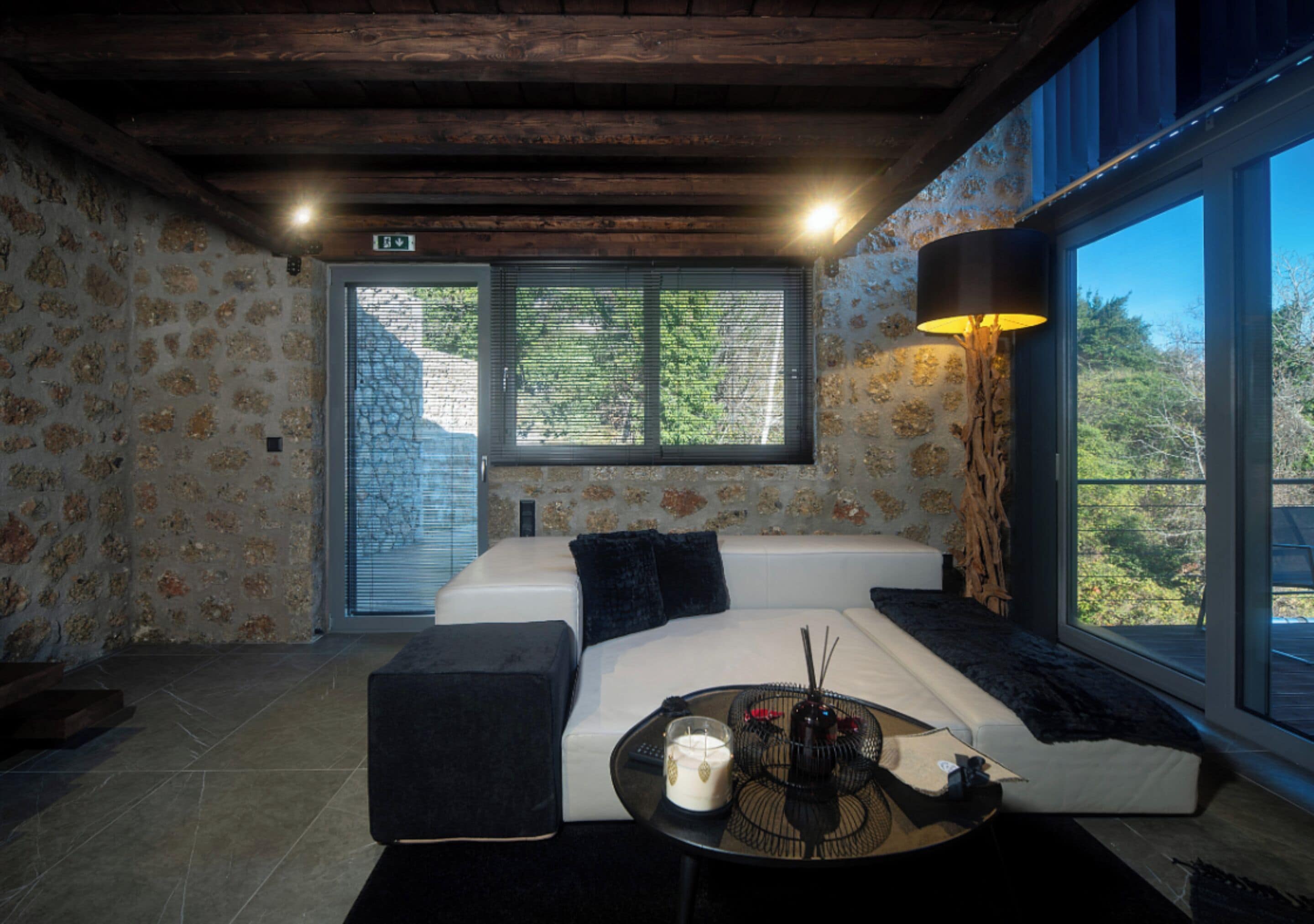 A room with a large window, a sofa, a table with candles, and a lamp.