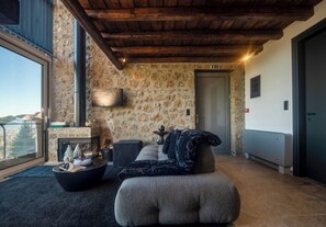 A cozy living area with a stone wall, a fireplace, a sofa, and a view through a large window.