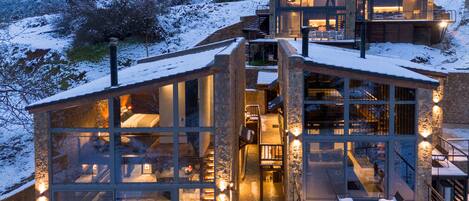 A modern glass house with multiple levels, connected by a staircase, set in a snowy landscape.