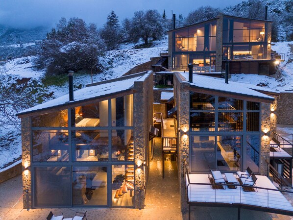A modern glass house with multiple levels, connected by a staircase, set in a snowy landscape.
