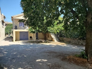A residential building with a paved driveway, a tree in the foreground, and a stone wall. - Gite du Plateau, House for 6 People (Saint-Remèze)