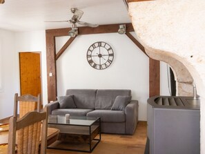 A living room with a grey sofa, a glass coffee table, a wooden chair, a wall clock, and a ceiling fan. - Gite du Plateau, House for 6 People (Saint-Remèze)