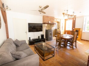 A living room with a sofa, a coffee table, a TV, a fireplace, and a dining area with chairs and a table. - Gite du Plateau, House for 6 People (Saint-Remèze)