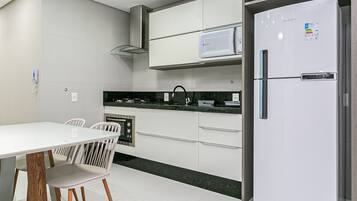 A modern kitchen with a white refrigerator, a microwave, and a built-in oven. There is a dining table with chairs and a black countertop.