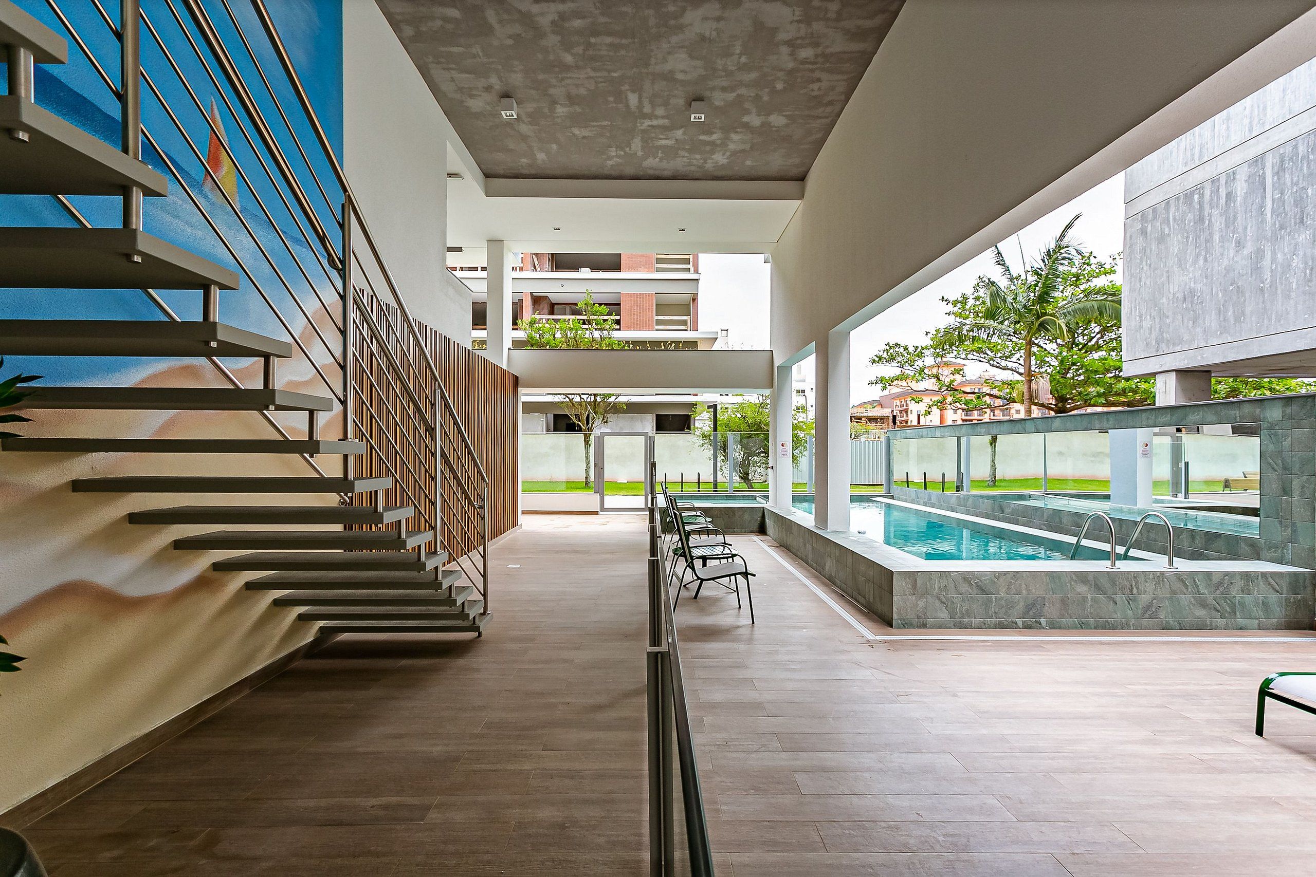 Uma área moderna de piscina interna com uma escada à esquerda e vista para edifícios externos.