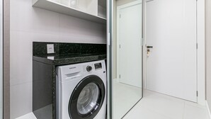 Un lavadero moderno con una lavadora Samsung, una puerta de cristal y una puerta blanca al fondo.
