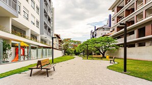 Un sendero que lleva a un parque infantil con tobogán y estructuras para escalar, bancos y árboles.