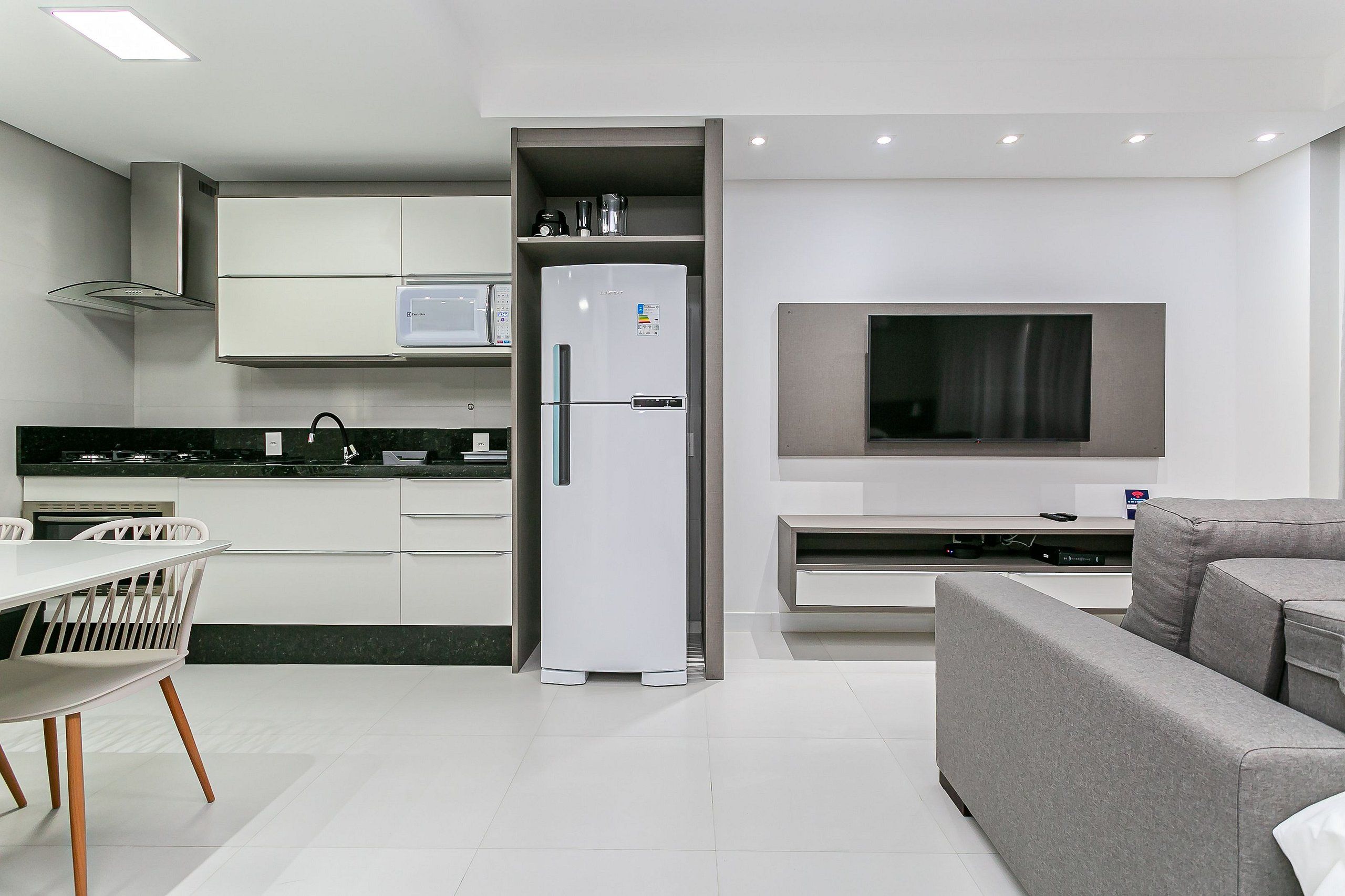 Una cocina moderna con armarios blancos, microondas integrado y un sofá gris.