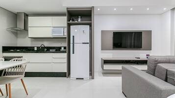 Una cocina moderna con armarios blancos, microondas integrado y un sofá gris.