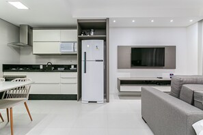 A modern kitchen with white cabinets, a built-in microwave, and a grey sofa. - Complete Studio 3 Minutes From the sea Jrr205 (Florianópolis)