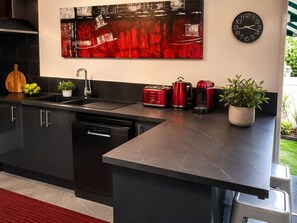 A modern kitchen with a black countertop, stainless steel appliances, and a red abstract painting above the sink.