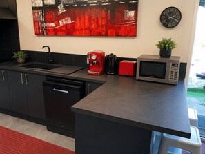 Una cucina moderna con un piano di lavoro nero, una macchina da caffè rossa, un forno a microonde argentato e un orologio nero appeso al muro.