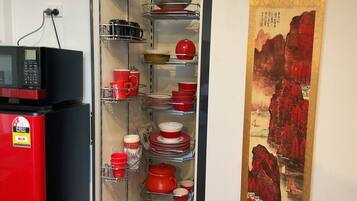 Une cuisine avec un réfrigérateur rouge, un four à micro-ondes et des étagères remplies d’assiettes rouges et blanches.
