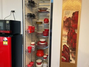 A kitchen with a red refrigerator, a microwave, and shelves with red and white dishes.