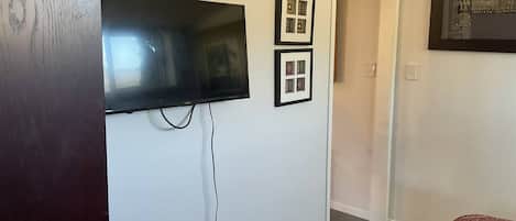 A room with a flat-screen TV mounted on the wall, a door leading to another room, and a framed picture collection on the wall.