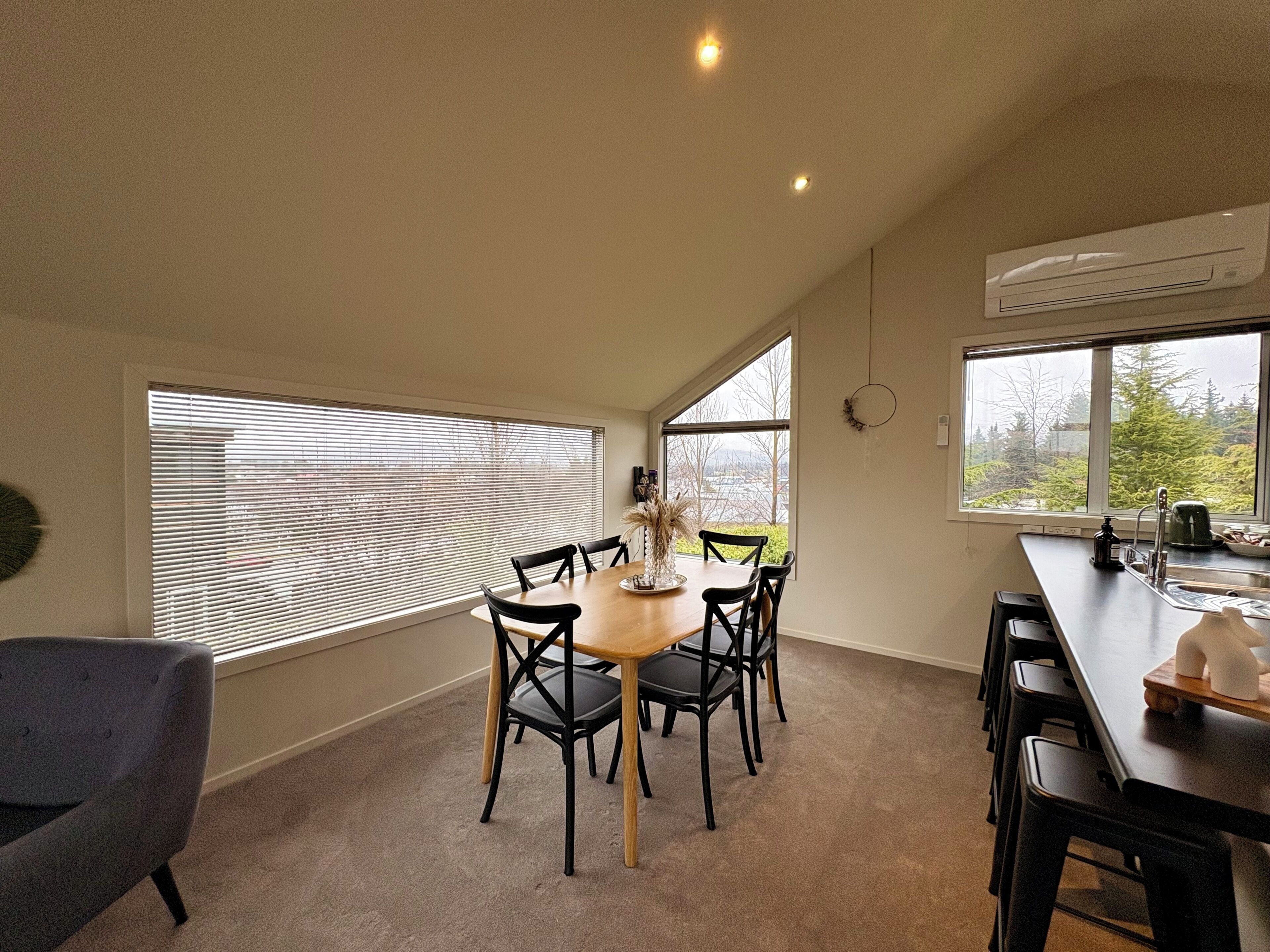 A dining area with a round table, chairs, and a view through large windows.