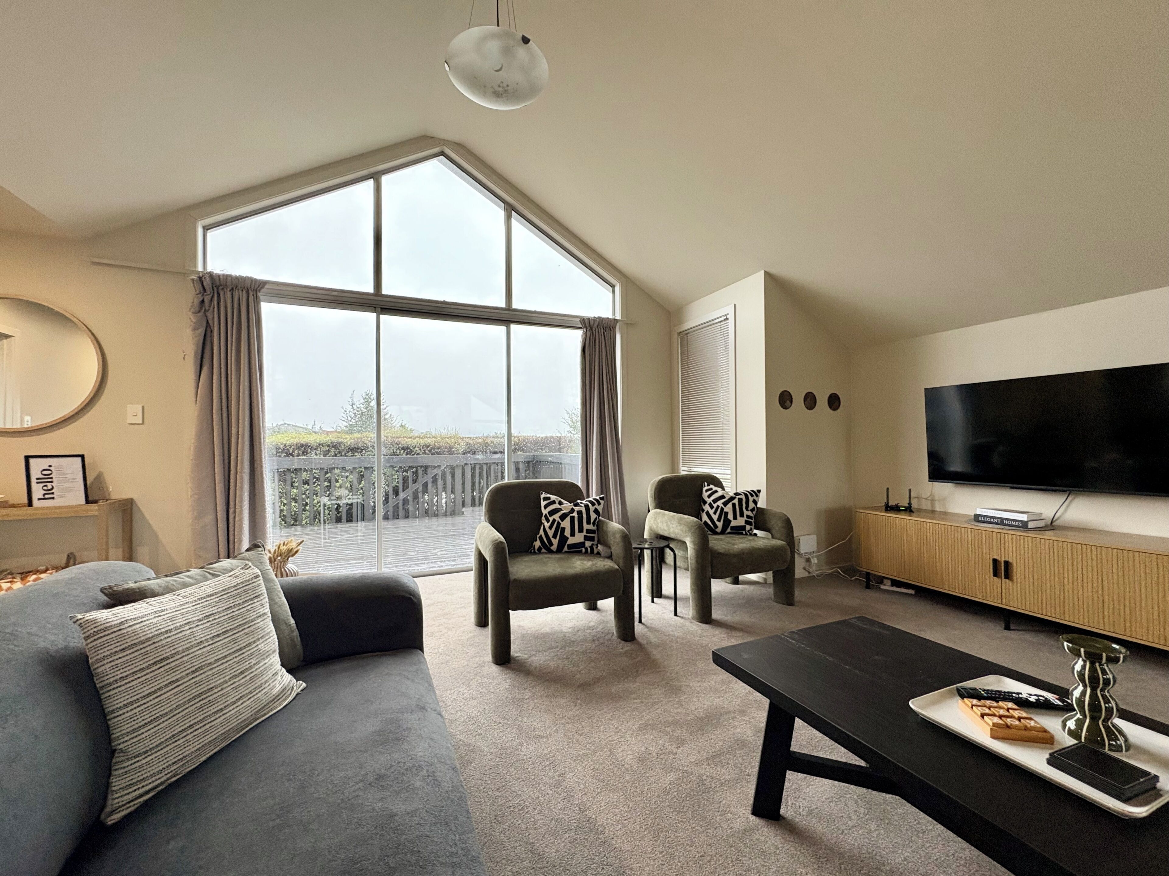 A modern living room with a large window, a flat-screen TV, and a sofa.