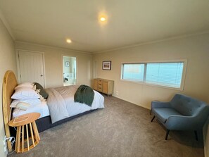 A bedroom with a bed, a chair, a dresser, a window, and a door. - Sunny Wānaka Home with Stunning Mountain Views (Wānaka)