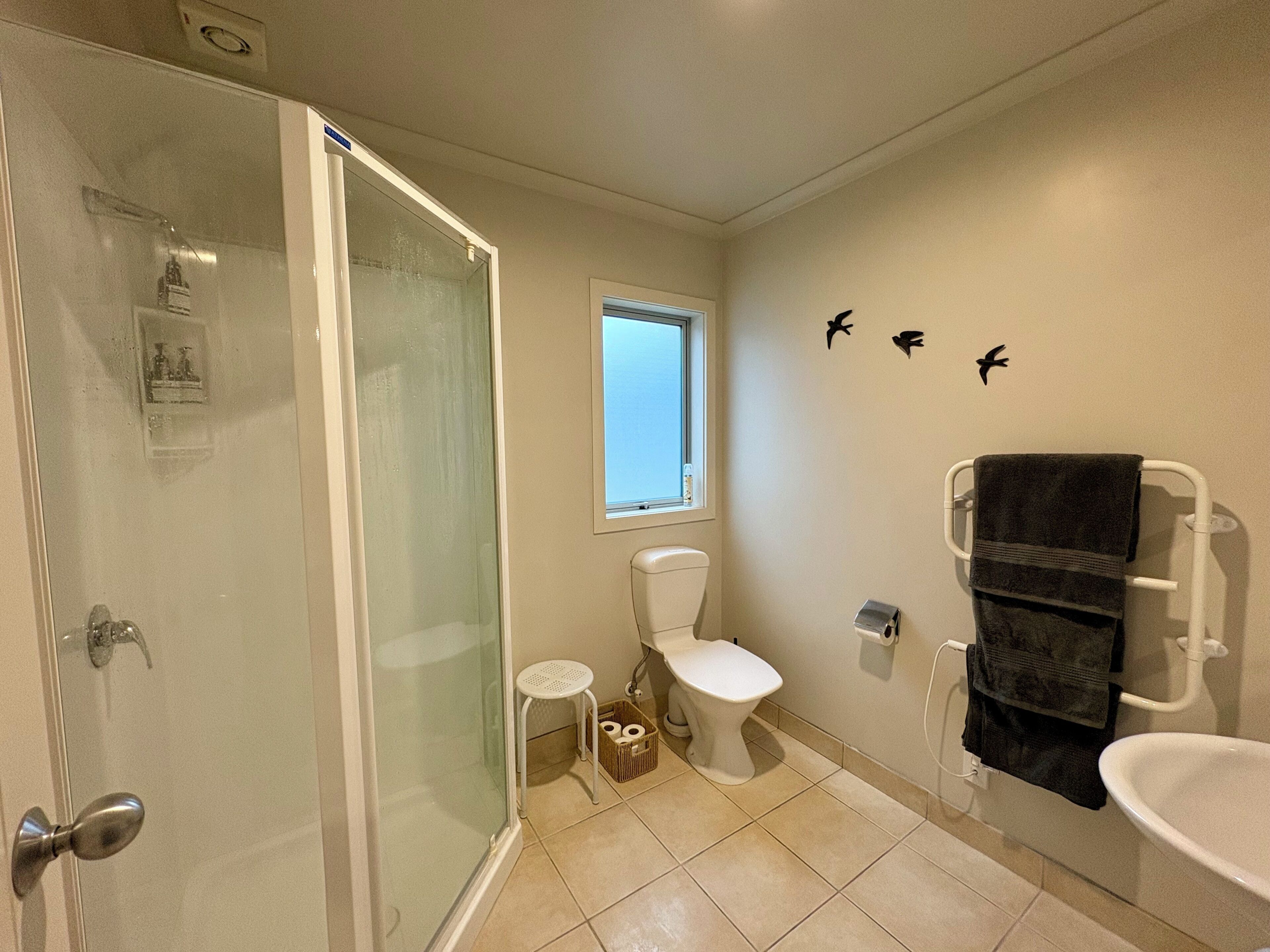 Baño con cabina de ducha de vidrio, inodoro, ventana pequeña y bañera con toallero.
