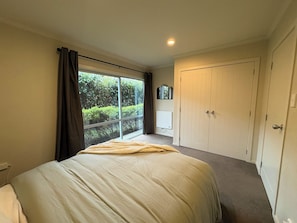 Ein Schlafzimmer mit einem großen Bett, einem Fenster mit Vorhängen, einem Heizkörper und einem Kleiderschrank.