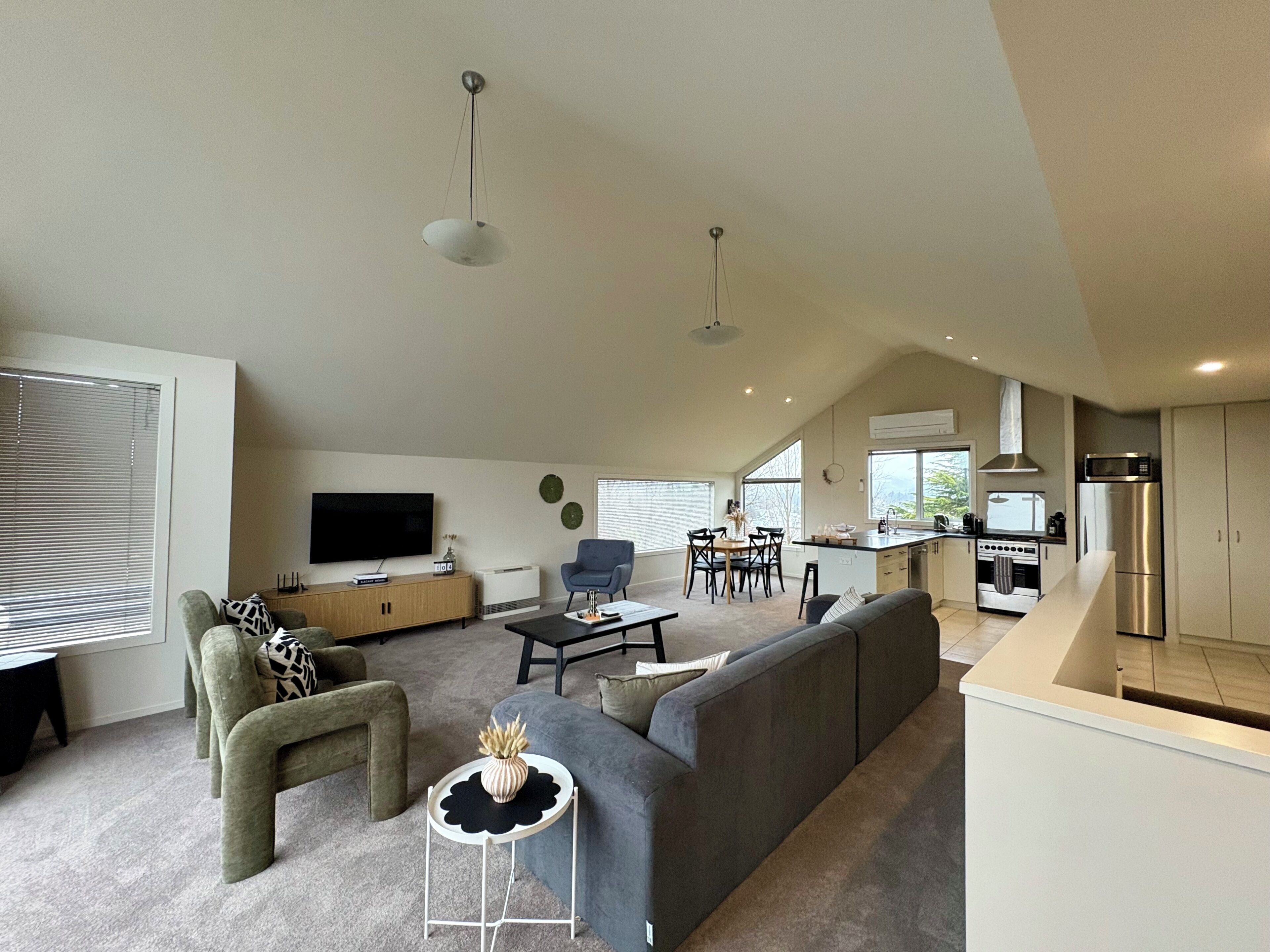 Una sala de estar moderna con sofá, televisión y comedor con sillas y mesa.