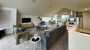 Een moderne woonkamer met een bank, een televisie en een eethoek met stoelen en een tafel.