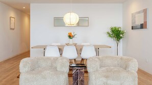 Uma área de jantar moderna com uma mesa de madeira, cadeiras brancas, um tapete macio e um lustre.
